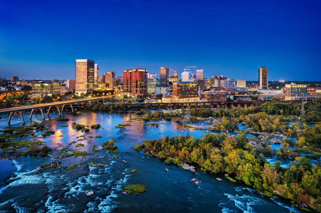 Downtown Richmond skyline aerial at dusk with 9th street bridge, James River, rapids, and islands in the foreground.